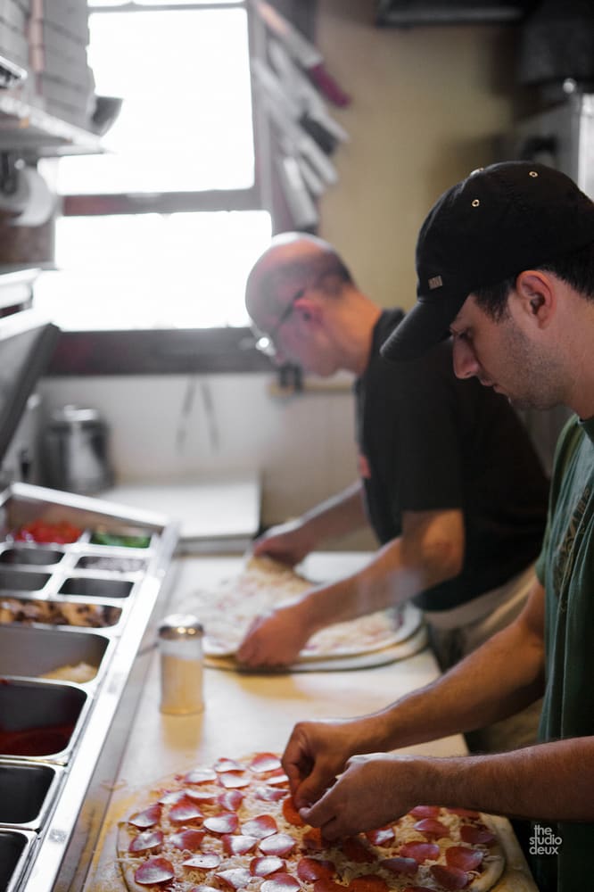 Two cooks topping a pizza at the prep counter