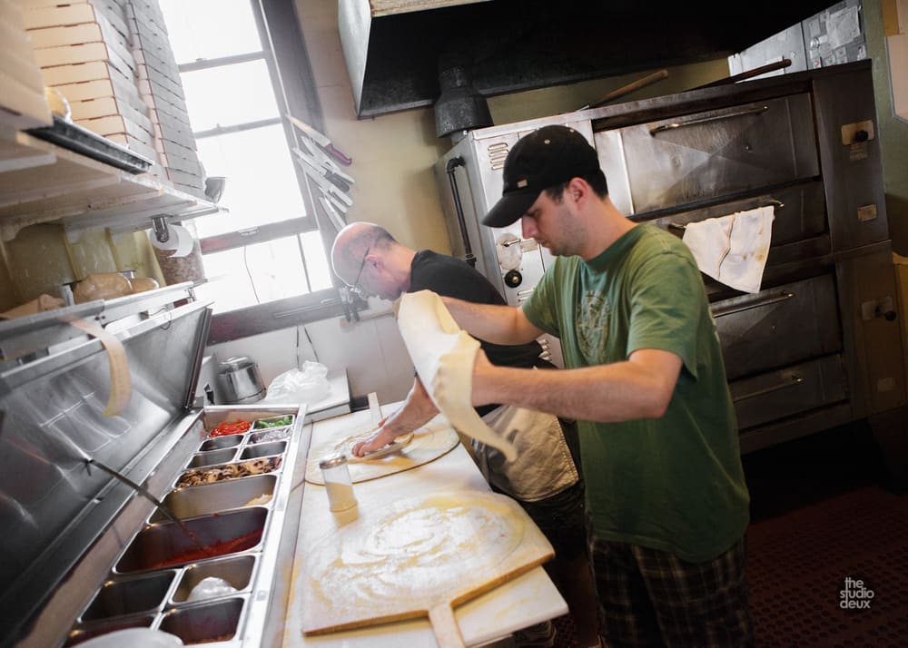 Two cooks shaping pizza dough in front of the ovens