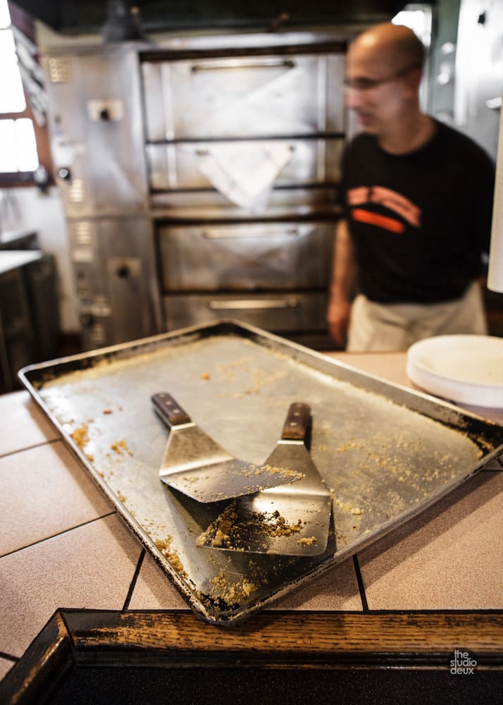 Two pizza spatulas on a cornmeal-dusted baking tray at the counter