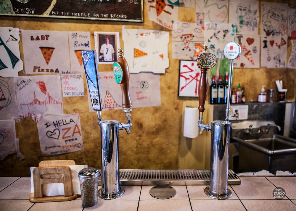 Beer taps at the counter, under a wall of pizza drawings