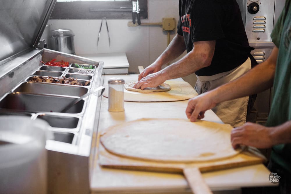 Stretching pizza dough on wooden peels at the topping station