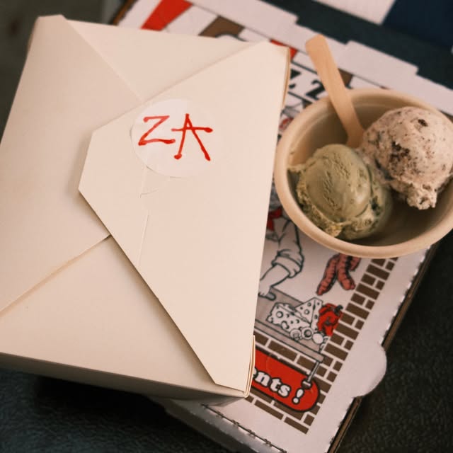 A cup of Aces ice cream beside a pizza wrapped with a ZA sticker
