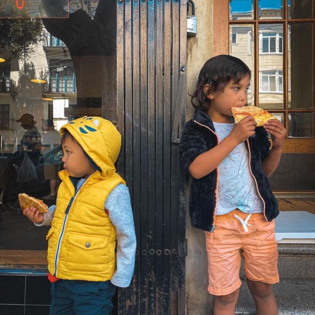 Two kids eating pizza slices on the sidewalk